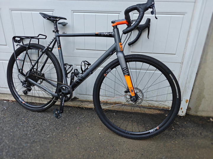 Dark gray NS Bikes gravel bicycle with a rear rack and orange accents