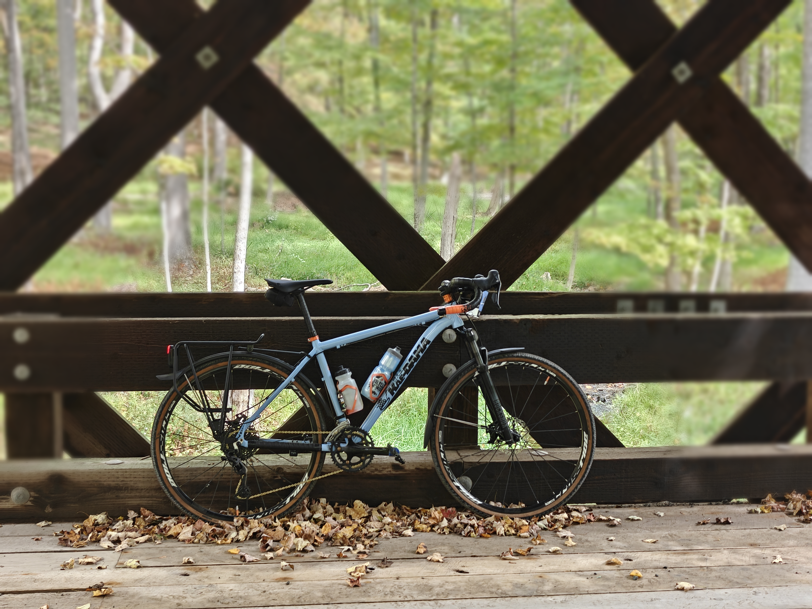 Blue Kaedama bicycle with orange accents and tan-wall tires on a wooded covered bridge