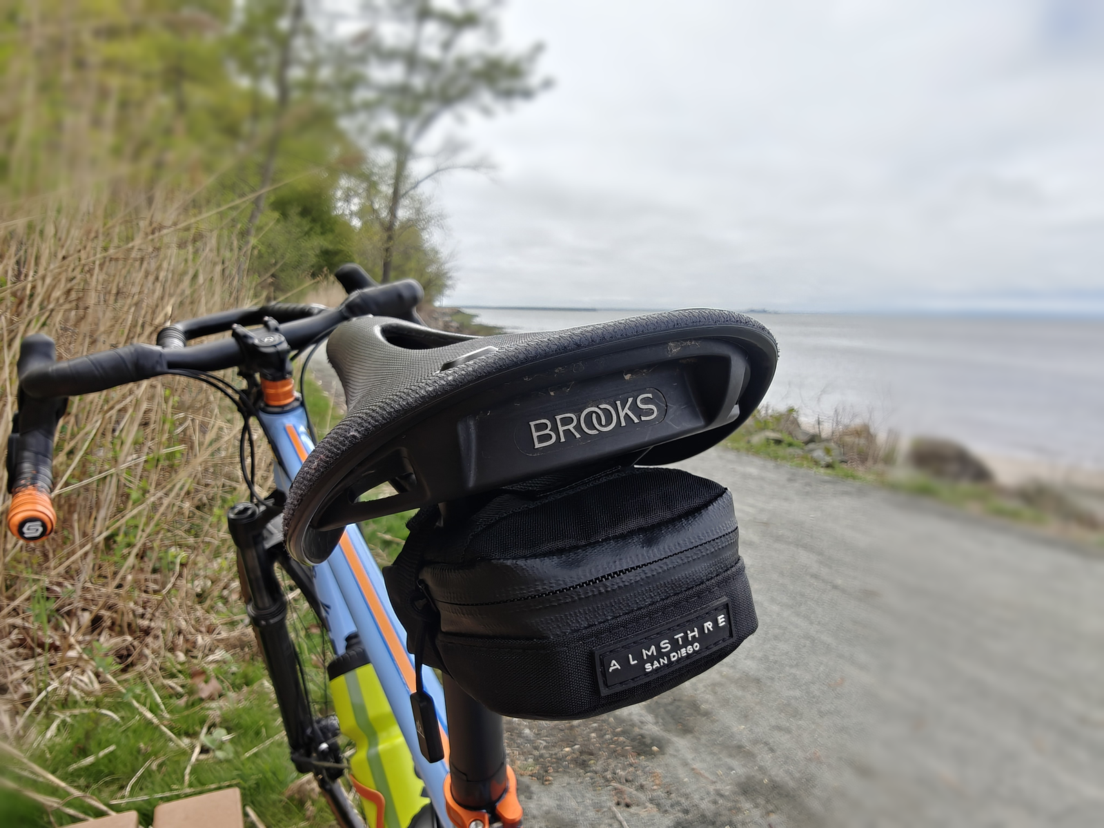 Saddle, seat bag, and orange finishing details on a blue Kaedama bike beside the water